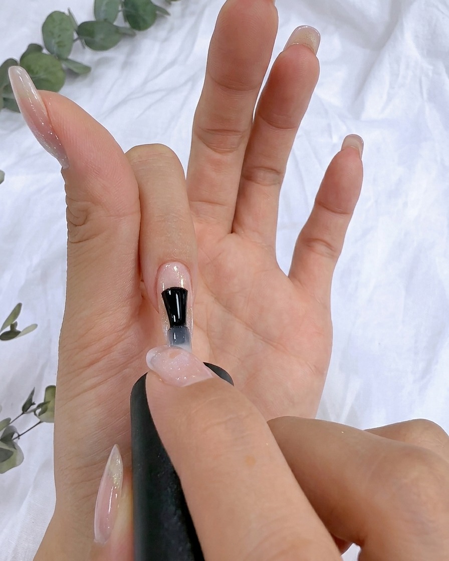 Un pincel aplicando gel de refuerzo transparente sobre la superficie de una uña natural.