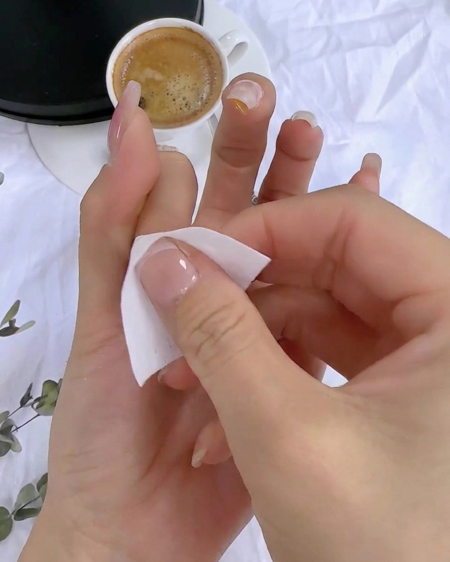 Una mano utilizando una toallita sin pelusa para limpiar el residuo pegajoso de la superficie de la uña curada.