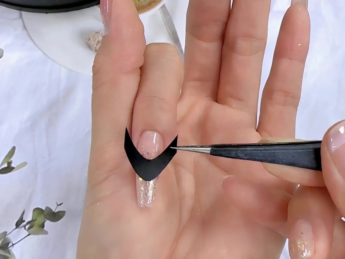 Unas pinzas colocando una pegatina guía francesa negra sobre una uña preparada.