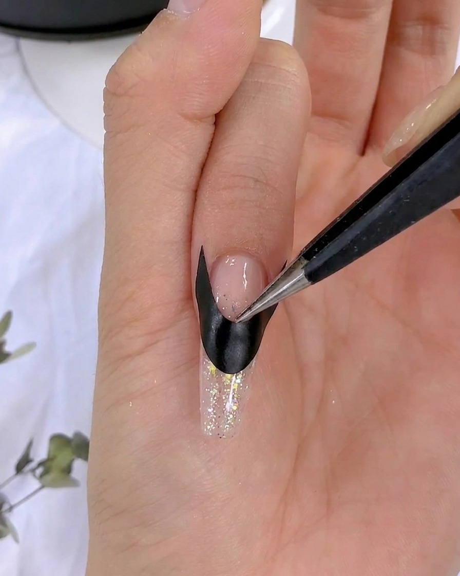 Unas pinzas alisando una pegatina francesa negra sobre una uña.