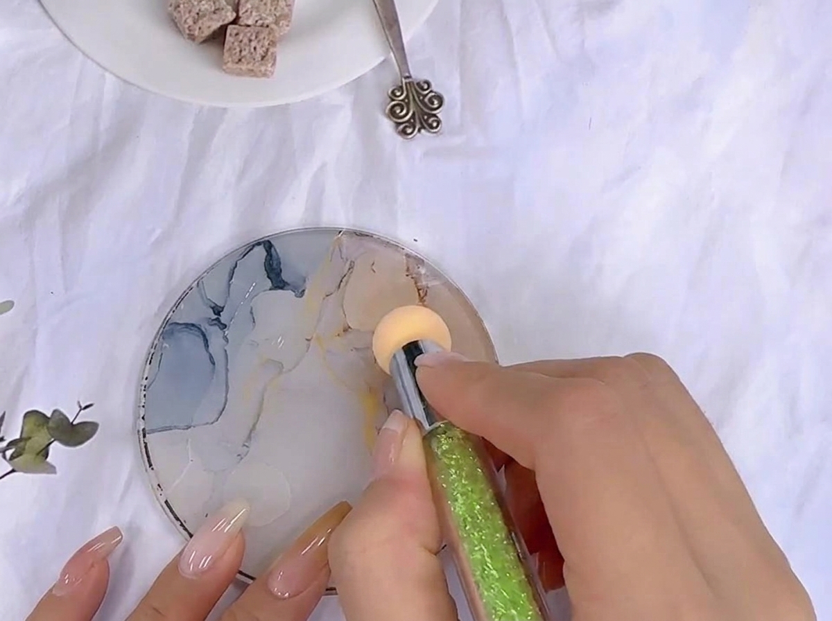 Una esponja tomando gel de color extendido sobre una paleta de mezclas de cristal estampada.