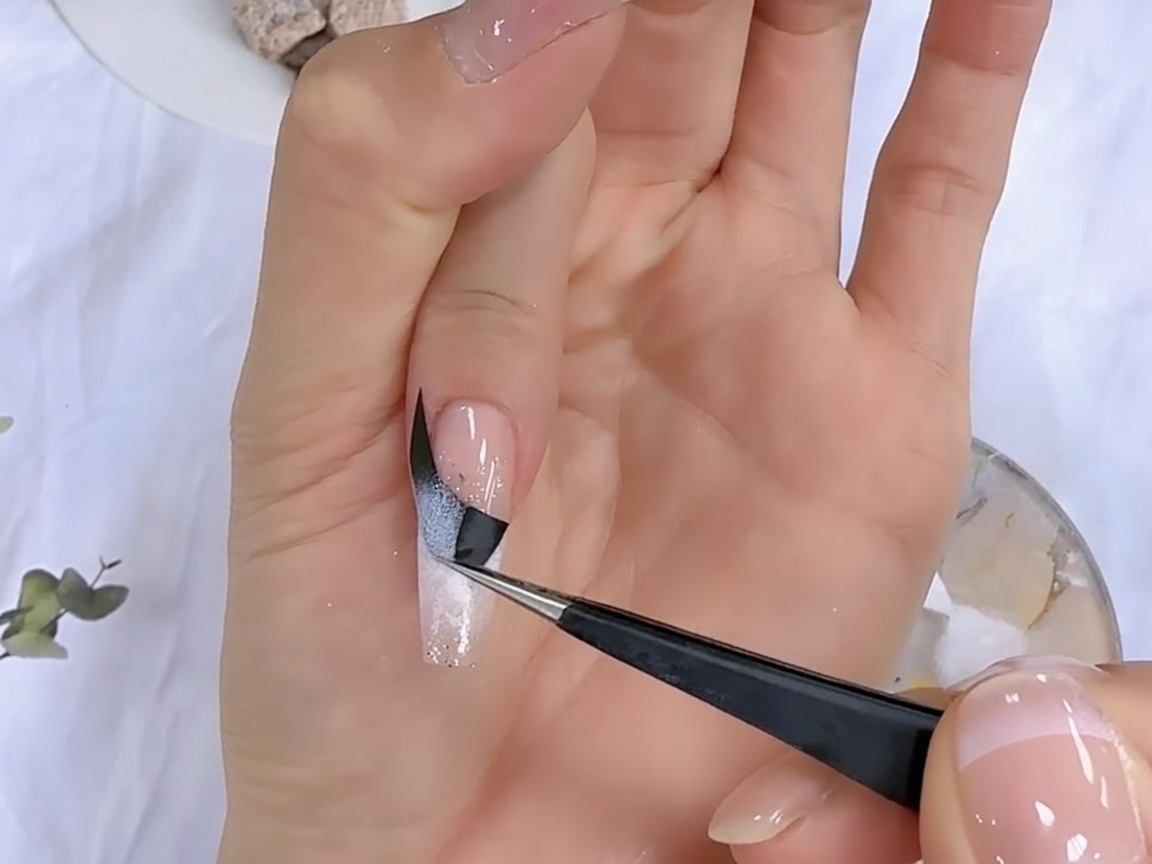 Unas pinzas despegando una pegatina guía francesa negra de una uña para revelar el diseño degradado debajo.