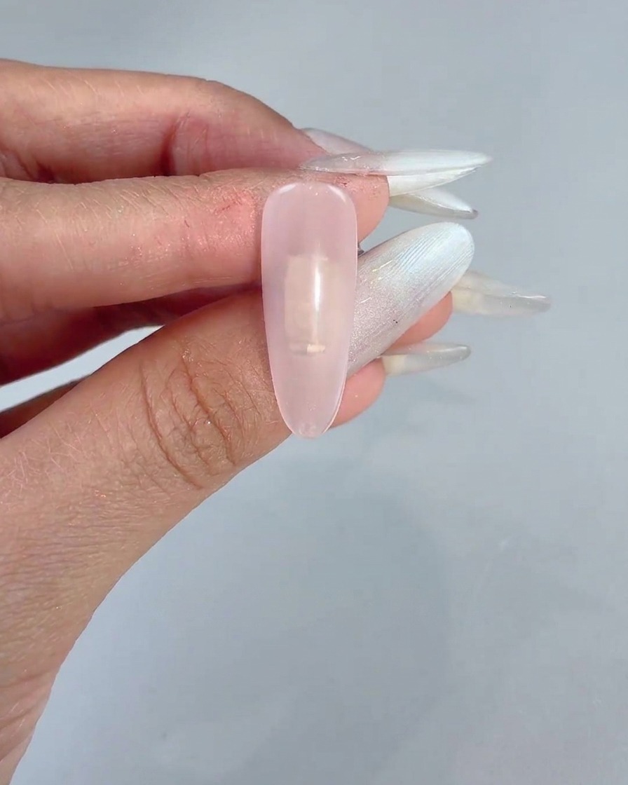Un bloque de esponja aplicando suavemente gel rosa en el centro de una uña con manicura transparente.