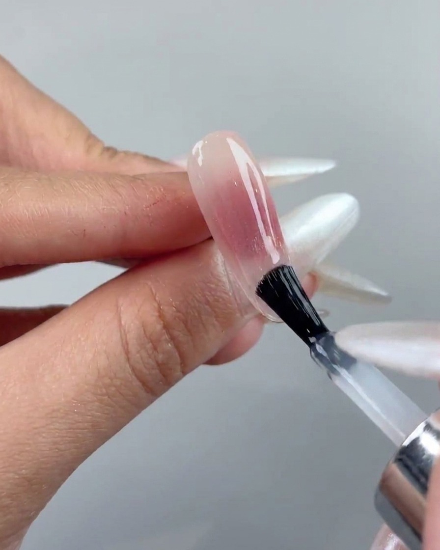 Un pincel de uñas aplicando una capa de top coat transparente sobre una uña de gel ojo de gato curada.