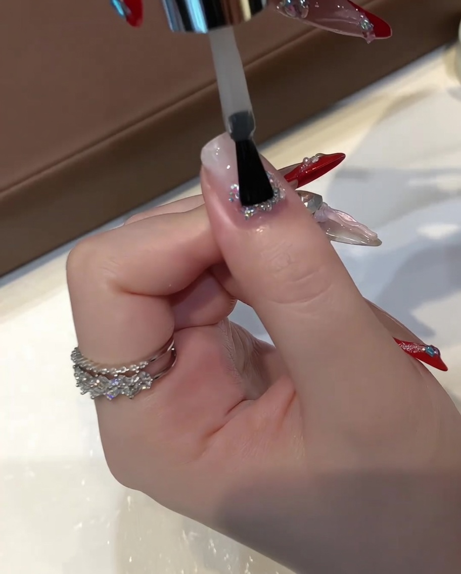 Un pincel plano de gel aplicando una capa gruesa de gel de construcción transparente nivelador sobre una uña con glitter encapsulado.