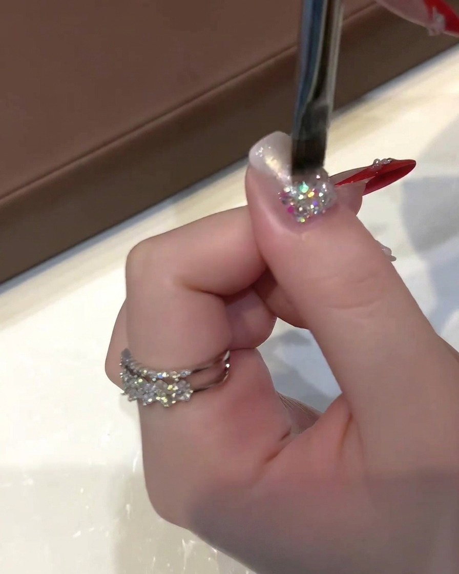 Una mano sosteniendo un pincel plano de gel aplicando esmalte cat-eye traslúcido sobre una uña con brillantina.