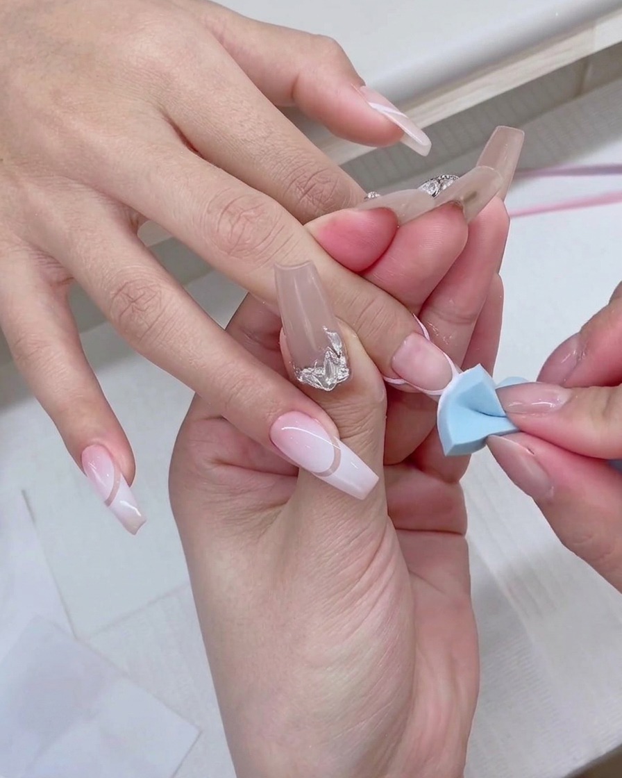Una esponja de maquillaje azul dando pequeños toques en la punta de la uña para crear un efecto degradado blanco.