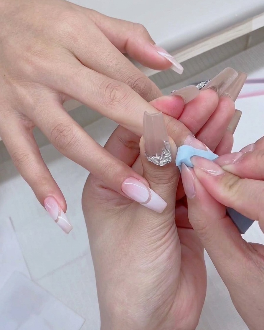 Un pincel de esmalte de gel aplicando producto blanco fresco directamente sobre el borde de una esponja azul.