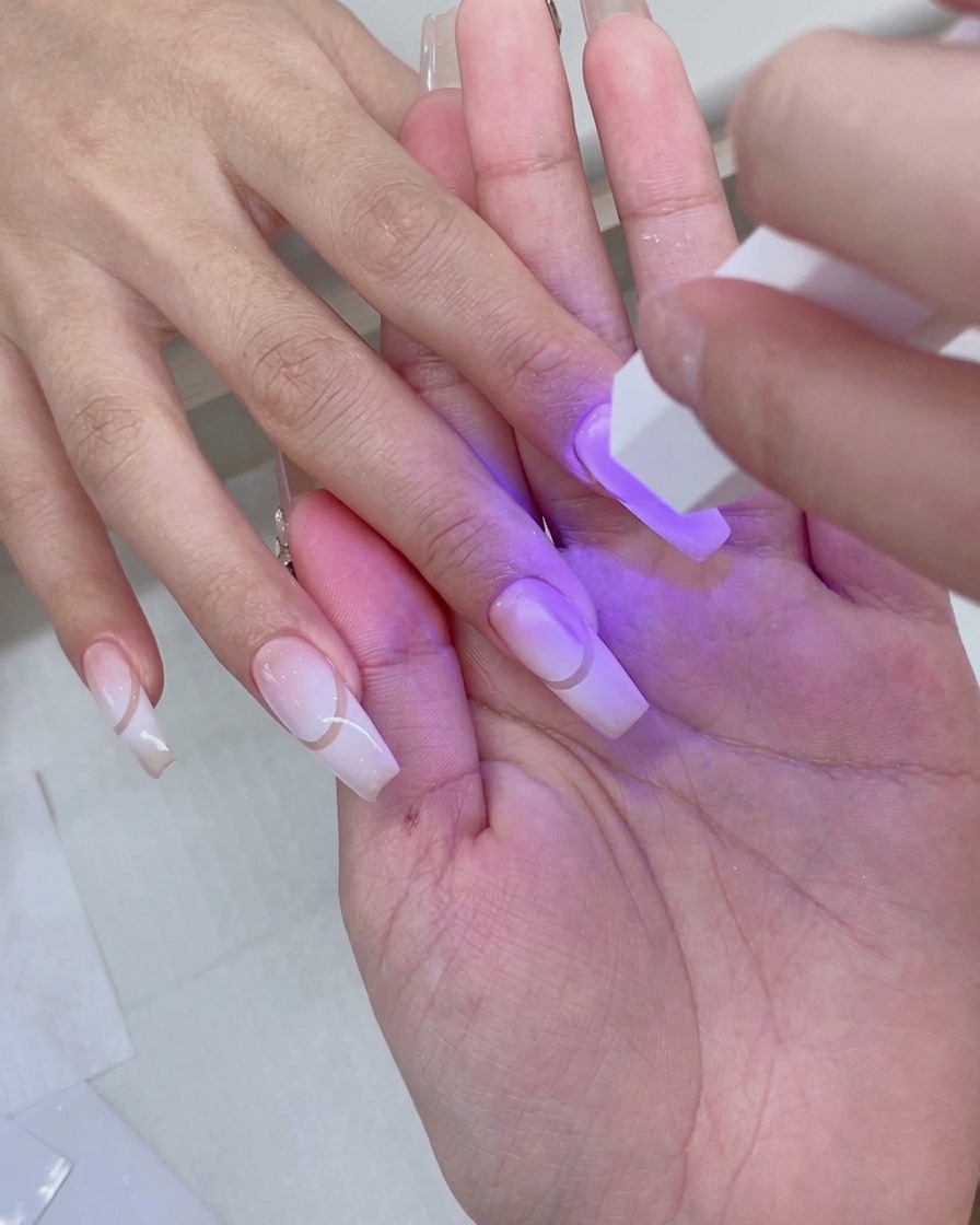 Una mano descansando dentro de una lámpara de uñas UV/LED rosa con luz morada iluminando las uñas preparadas con degradado.