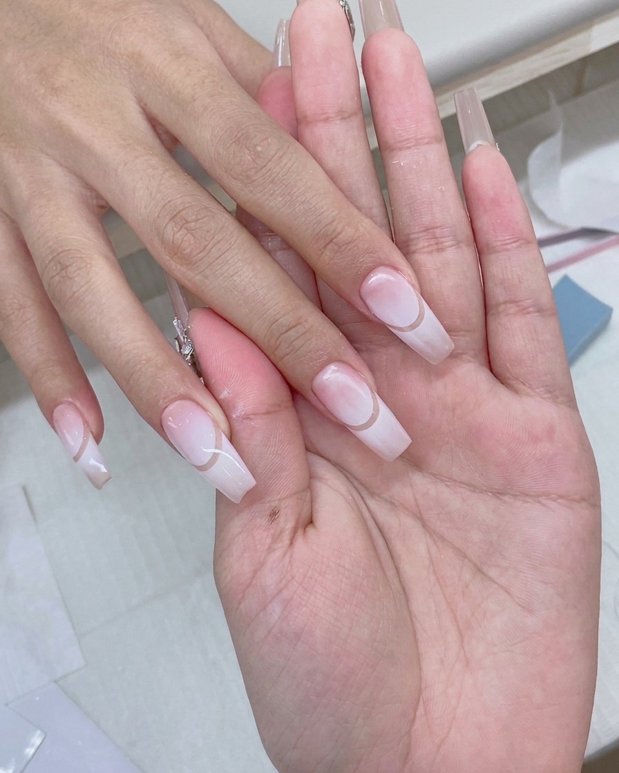 Un pincel aplicando un top coat transparente y brillante sobre un diseño de uñas degradadas terminado.