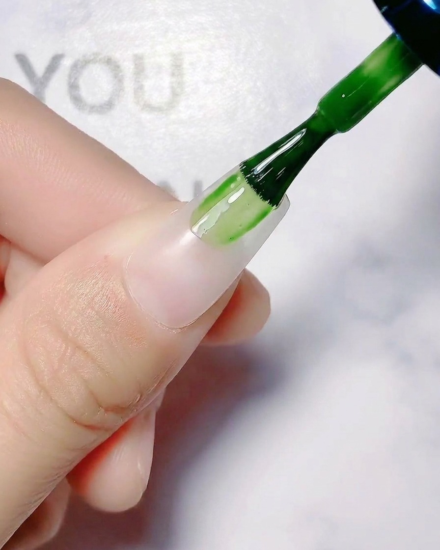 Un pincel de uñas aplicando una capa base blanca translúcida sobre una uña natural.