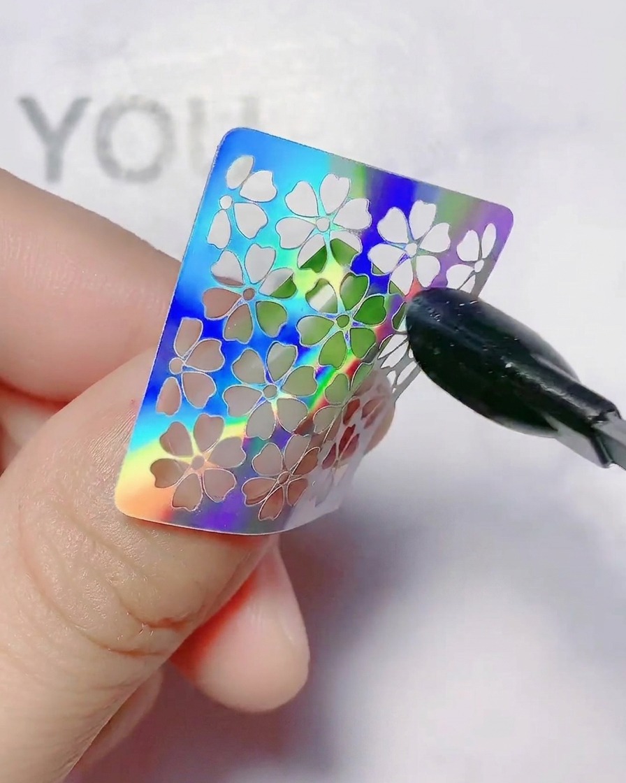 Una pegatina de flor hueca para uñas siendo presionada sobre una uña con degradado.