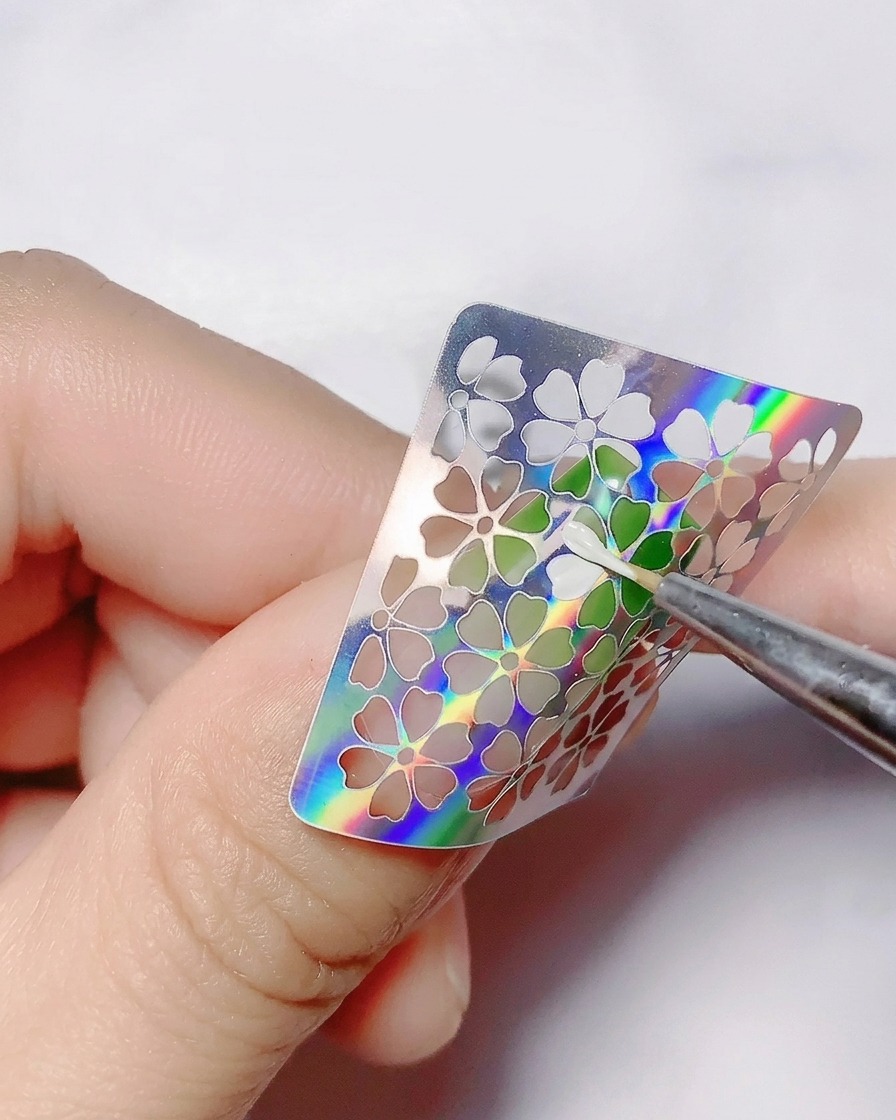 Un pincel fino aplicando gel de color blanco dentro de los recortes huecos de flores de una pegatina.