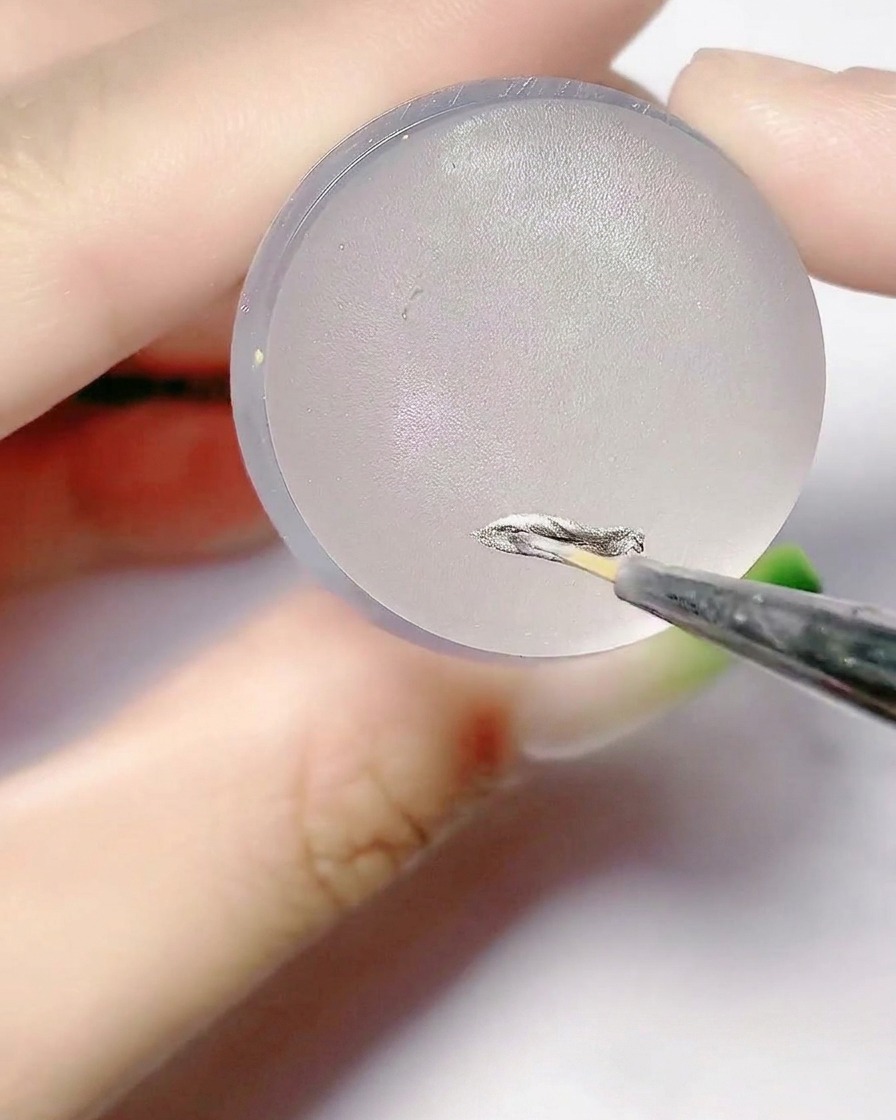 Un pincel fino aplicando gel plateado sobre la superficie plana de una almohadilla de sello de silicona.
