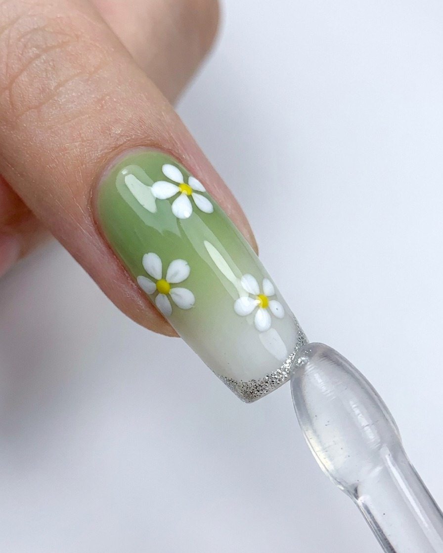 Una uña decorada con flores blancas siendo presionada contra un sello de silicona para aplicar una punta francesa plateada.