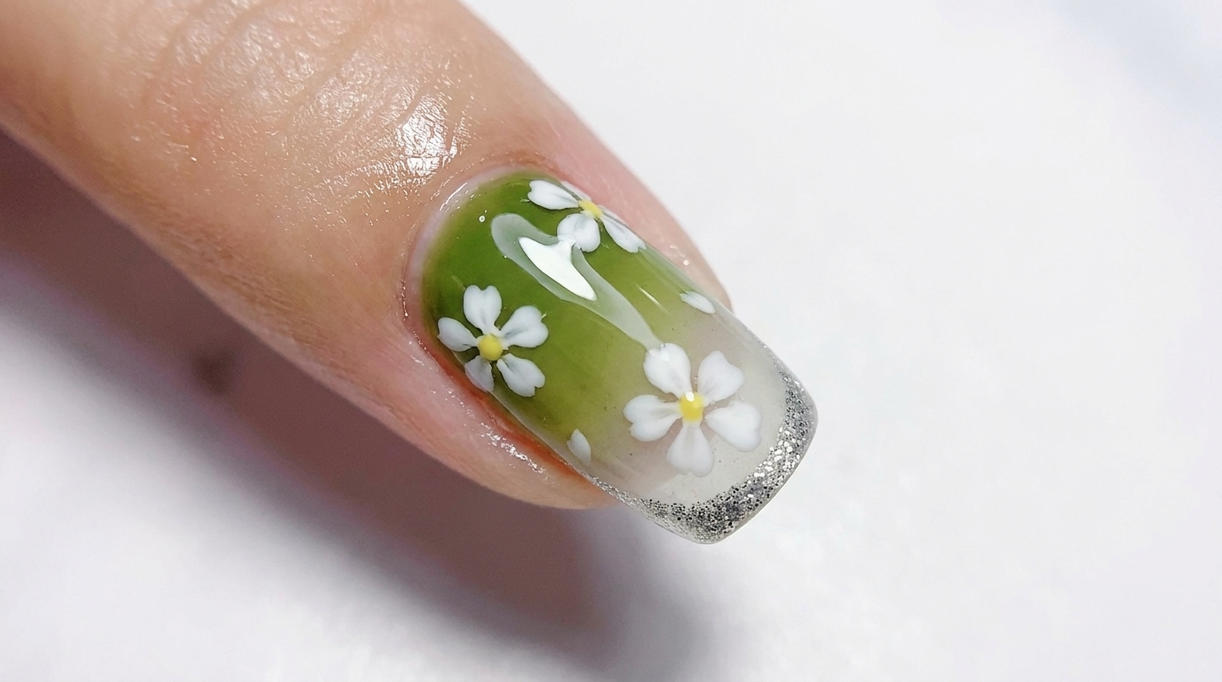 Uñas de gel con degradado brillante de verde oliva a blanco translúcido, con flores blancas de cinco pétalos y una fina punta francesa de purpurina plateada.