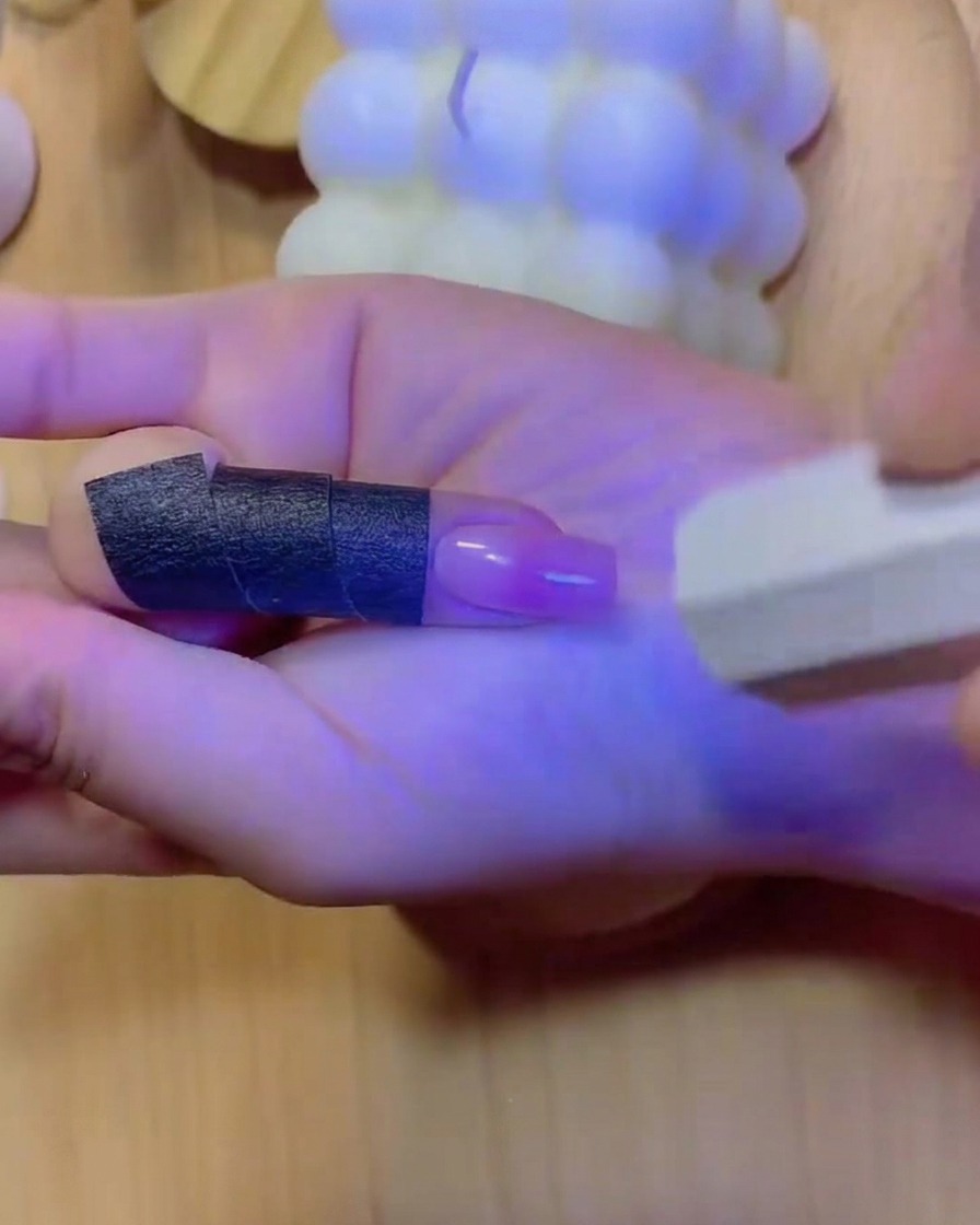 Una mano colocada dentro de una lámpara de uñas UV/LED con luz azul iluminando los dedos y la uña con degradado curado.