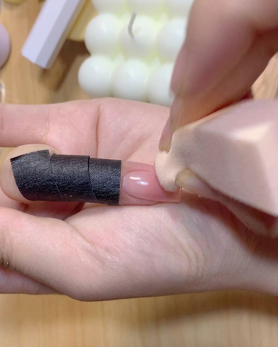 Una esponja de maquillaje aplicando color rosa sobre una uña manicurada para intensificar el degradado ombré.
