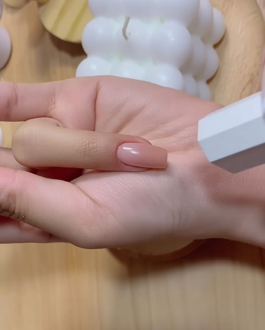 Una mano manicurada con una uña de degradado rosa intensificado posicionada cerca de una lámpara UV blanca.