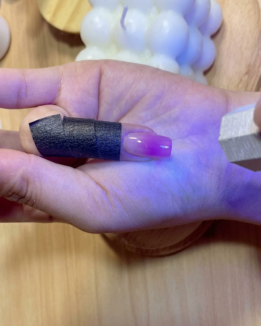 Una uña brillando bajo luz violeta UV/LED mientras se cura el gel de refuerzo aplicado.