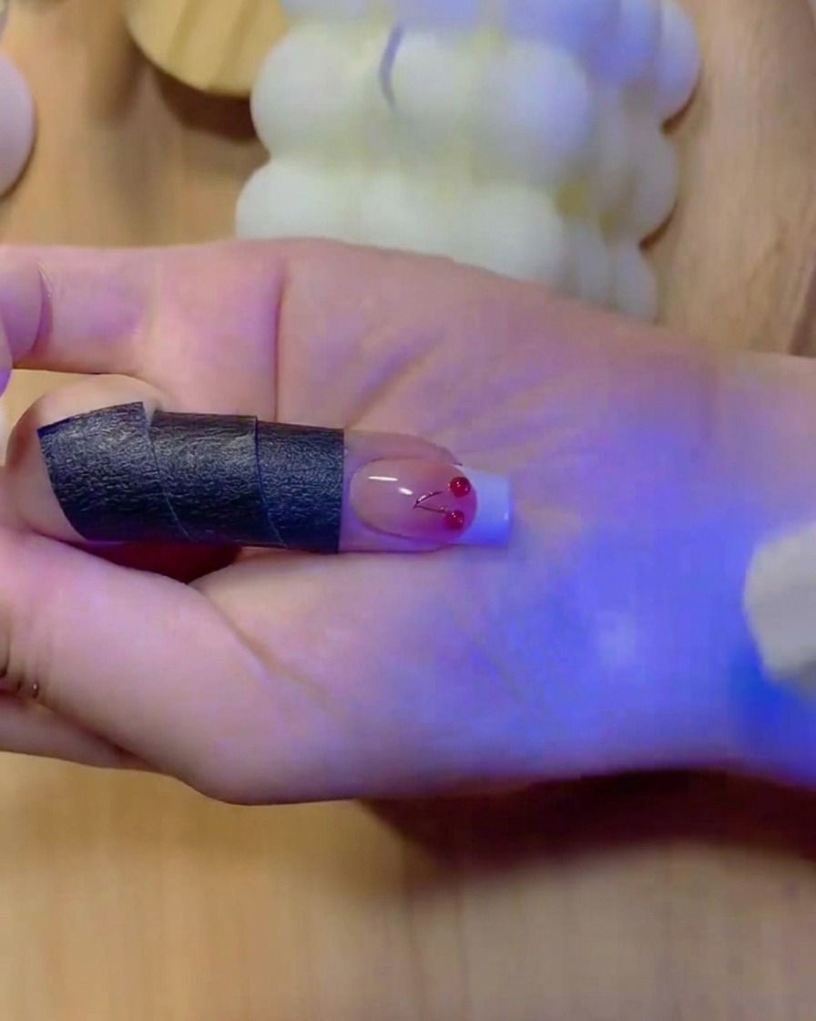Un pincel fino rellenando el color blanco sólido de una punta de manicura francesa en una uña con degradado.
