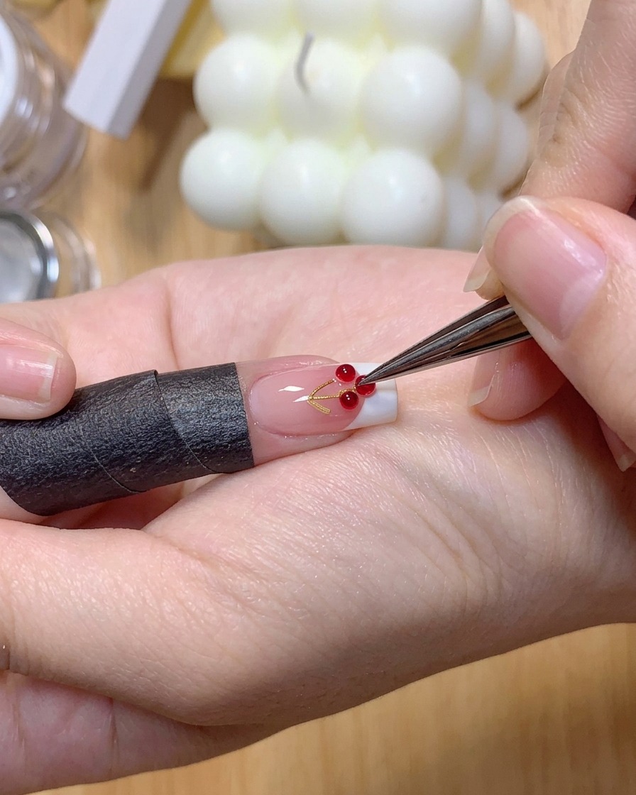 Un par de pinzas colocando dos pequeñas bolas de gel transparente 3D sobre la superficie de una uña con manicura francesa.