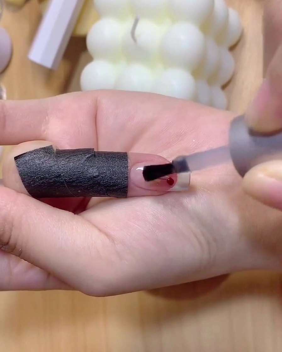 Un pincel de uñas fino aplicando esmalte de gel marrón claro para dibujar tallos delgados de cereza en una uña.