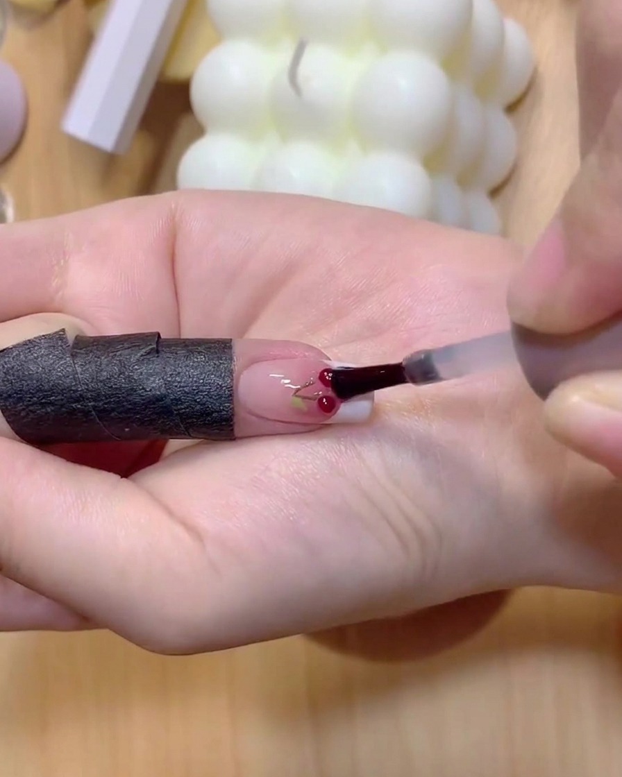Una uña con tallos de cereza pintados colocada bajo una lámpara de curado.