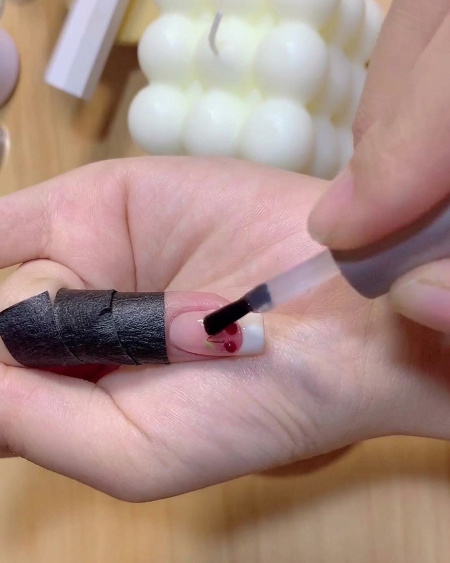 Un pincel aplicando esmalte de gel rojo translúcido sobre las bolas de cereza transparentes en 3D.