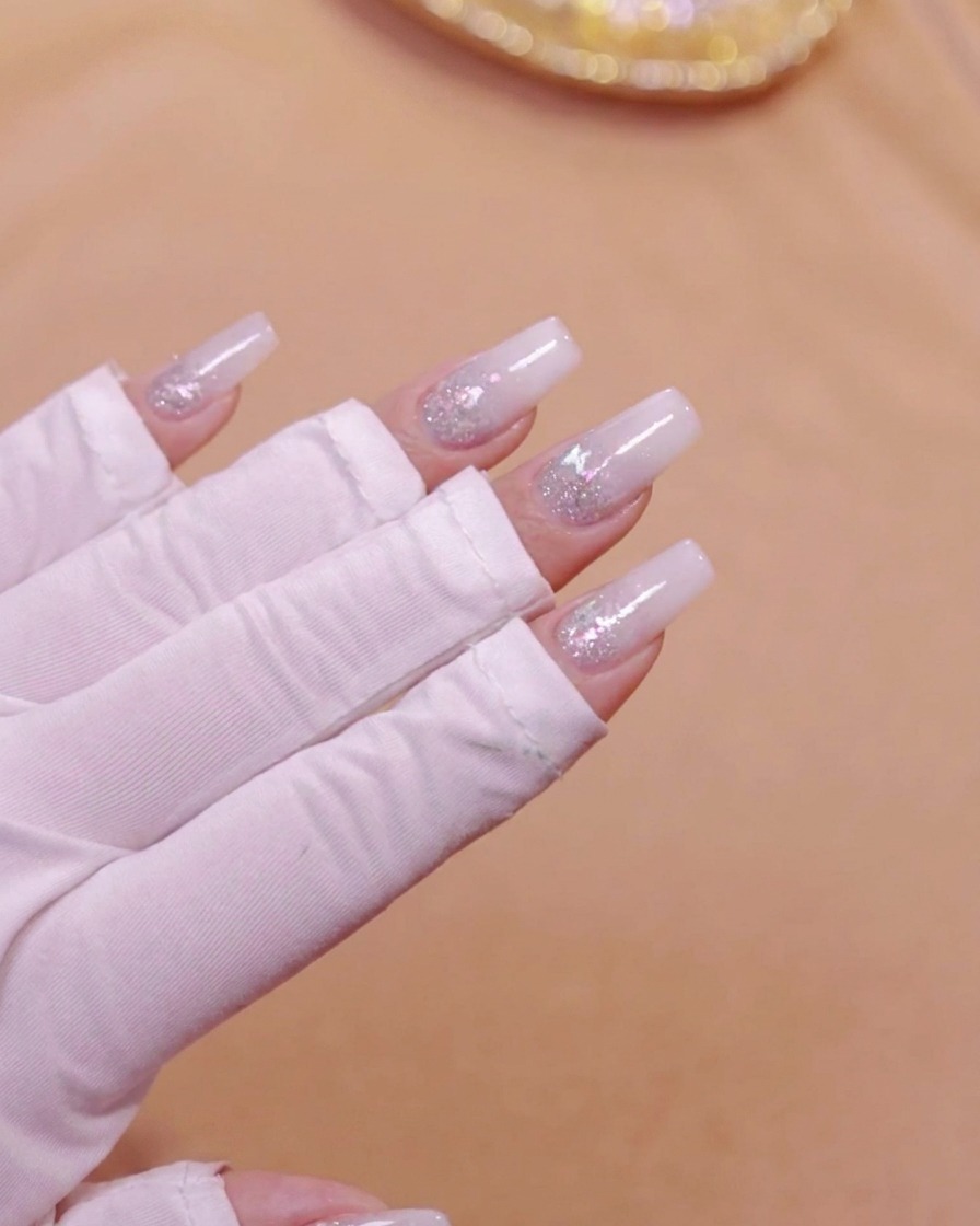 Una mano colocada dentro de una lámpara de uñas UV LED curando la capa degradada blanca lechosa.