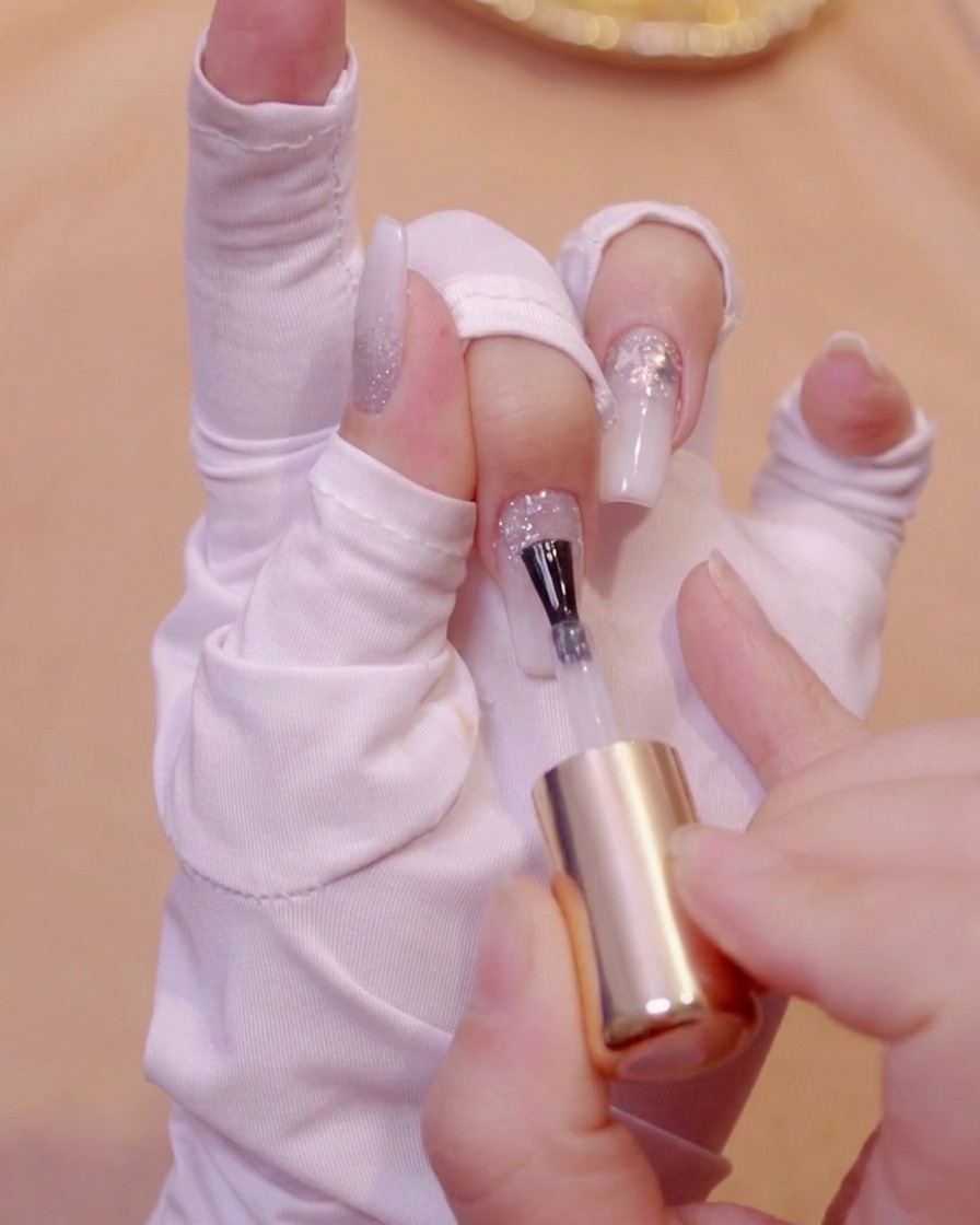 Un pincel aplicando gel nivelador transparente sobre la superficie texturizada de una uña con purpurina.