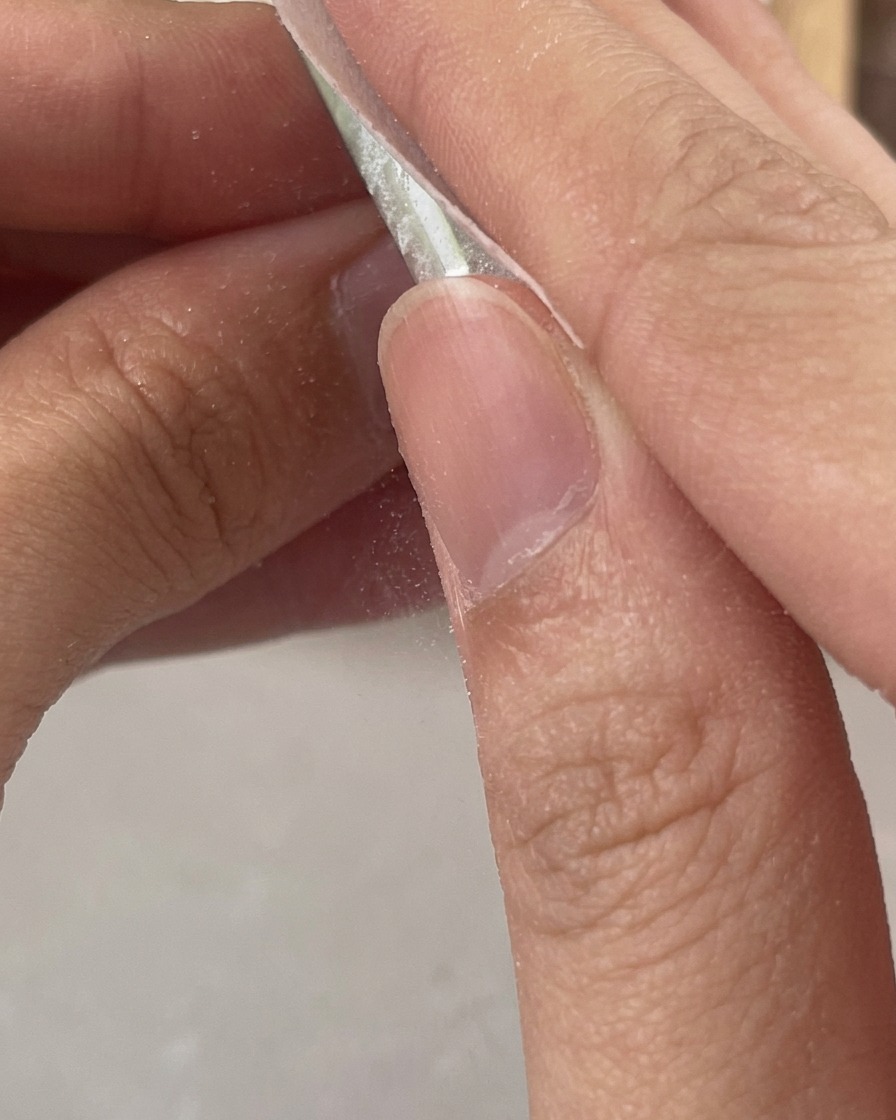Dedos usando una toallita sin pelusa para limpiar los residuos pegajosos de una uña de gel transparente recién curada.