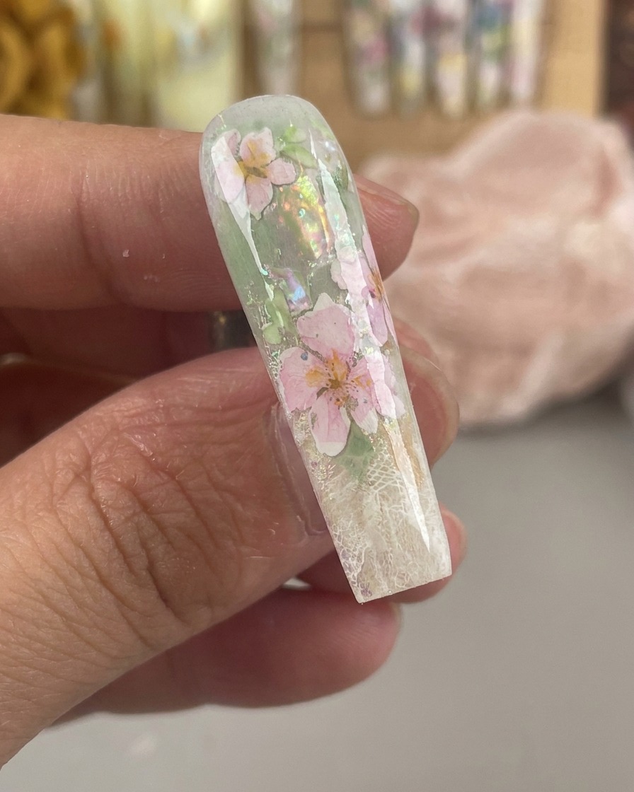 Una uña brillante y encapsulada que muestra flores de acuarela rosas y amarillas selladas bajo una gruesa capa de gel transparente.