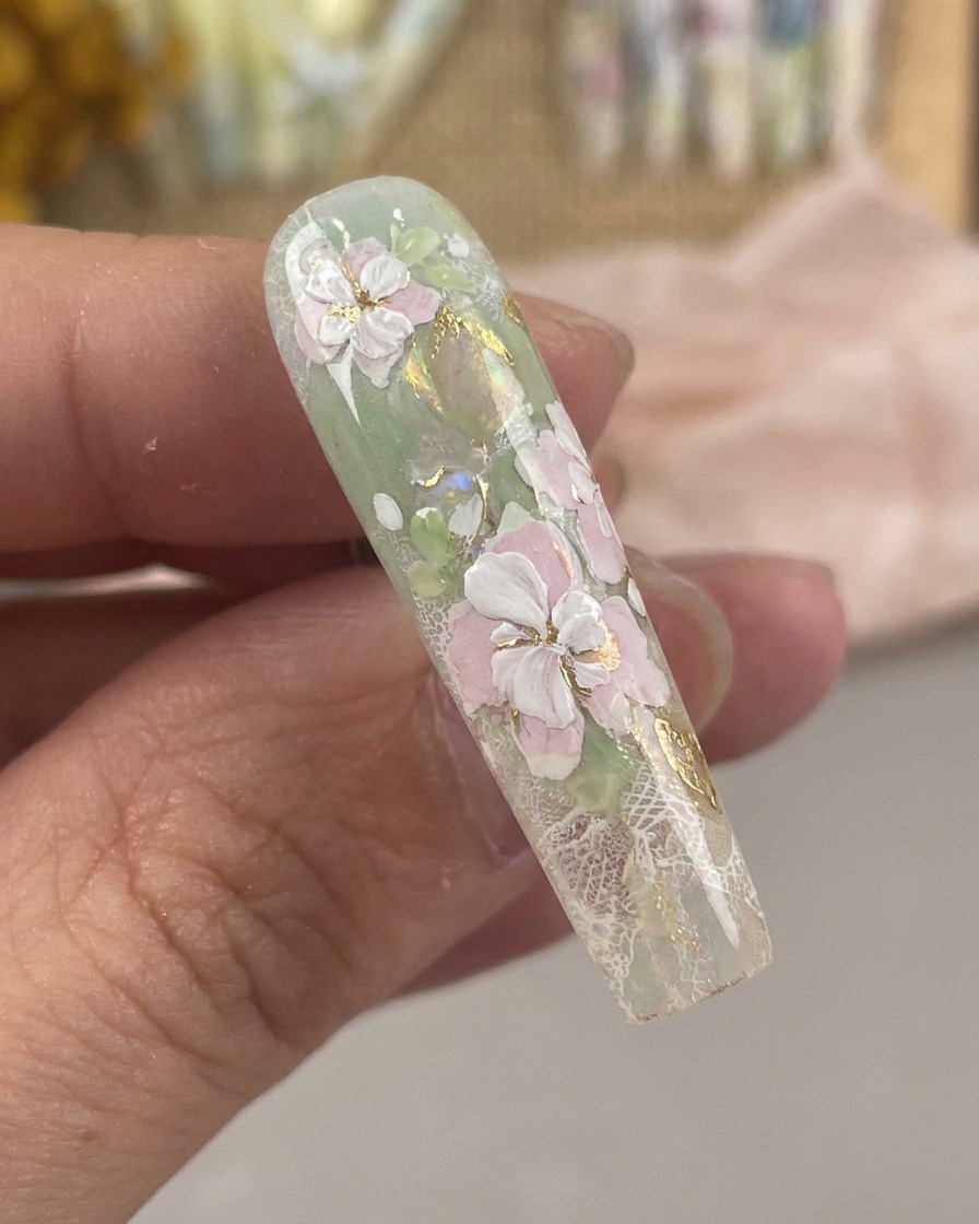 Vista de cerca de un pincel de nail art ultra fino dibujando detalles de estambres blancos y puntos centrales en un diseño floral.