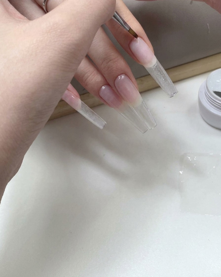 Pincel fino de nail art aplicando gel transparente en la parte inferior de una extensión de uña larga.