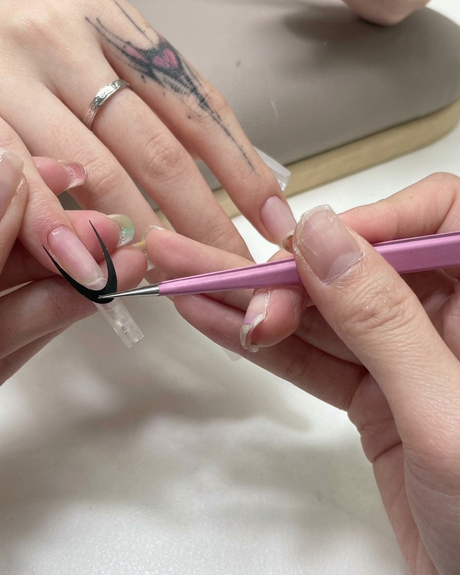 Pinzas rosas colocando una pegatina curva negra de guía francesa sobre una extensión de uña transparente.