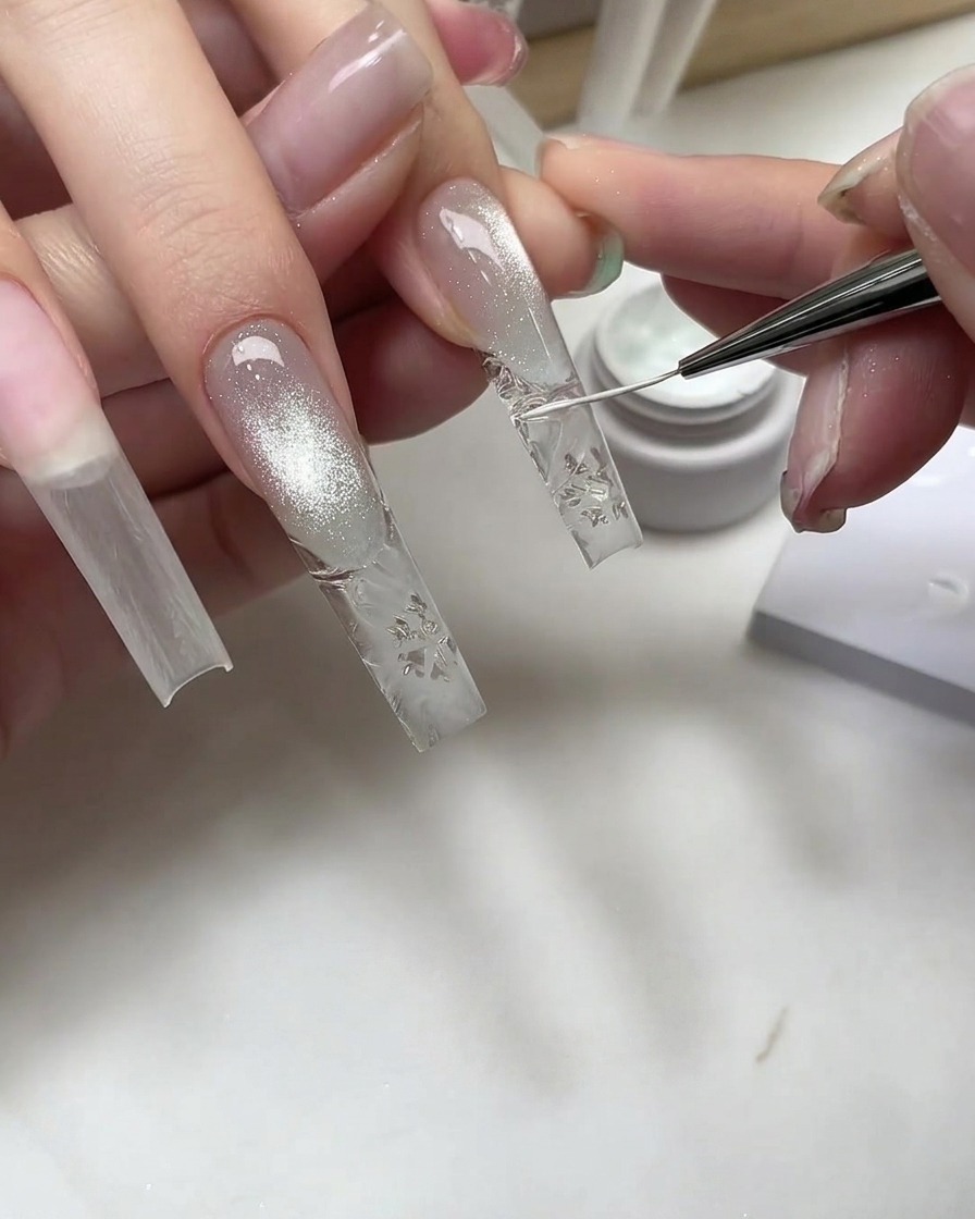 Pincel fino de nail art dibujando detalles de copos de nieve blancos sobre una extensión texturizada.
