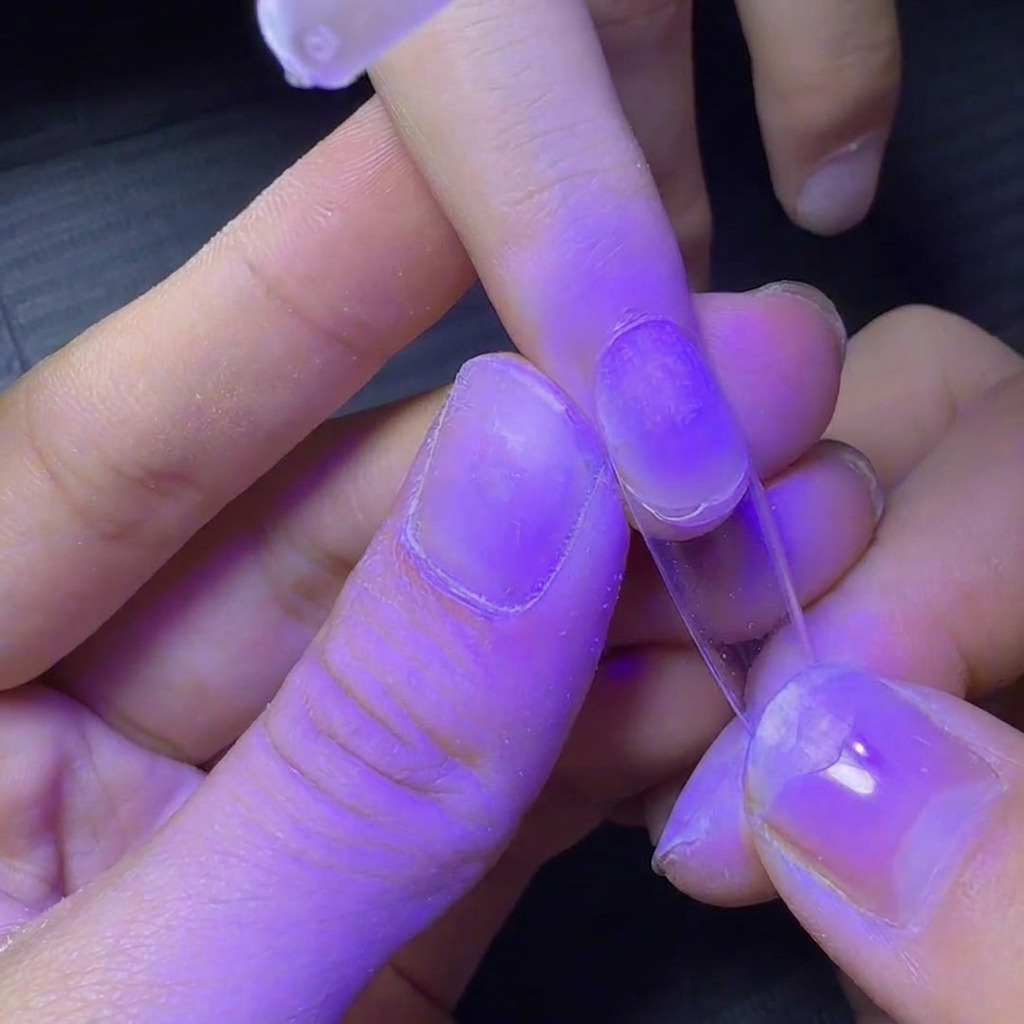 Una uña con un tip transparente bajo una lámpara UV morada para un curado rápido.
