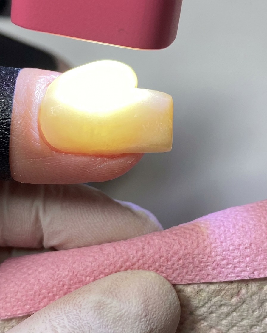 Una lámpara UV rosa de mano curando esmalte en gel amarillo en una uña.