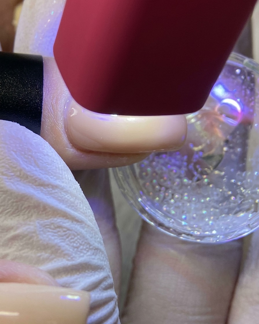 Una lámpara UV/LED roja de mano proyectando luz sobre una uña para curar un diseño de estrella blanca cubierto de purpurina.