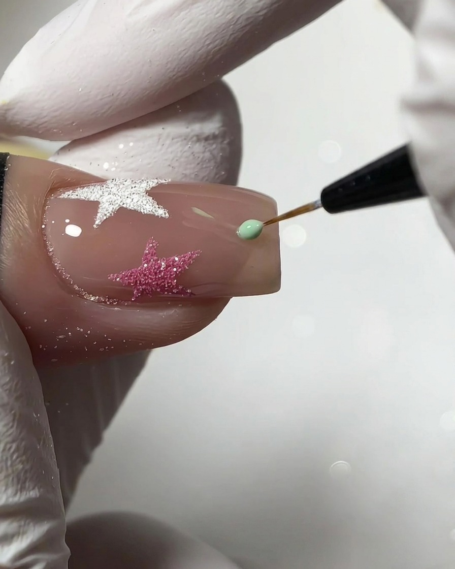 Un pincel liner fino aplicando una pequeña gota de gel verde menta para crear una forma de estrella en una uña nude.