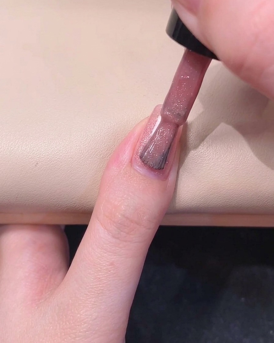 Un pincel de uñas pintando el lado derecho de una uña con esmalte en gel rosa brillante.