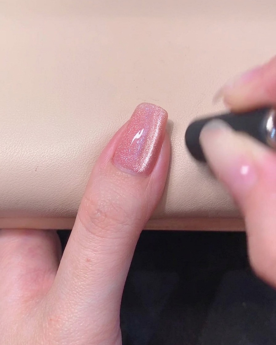Un primer plano de una uña de gel rosa con una raya brillante de ojo de gato magnético visible en la superficie de gel húmedo.