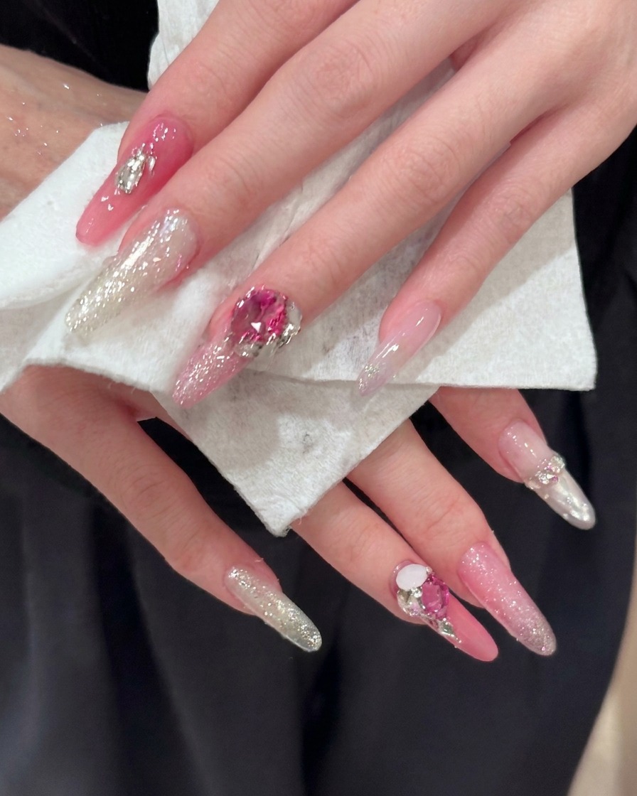 Un primer plano de uñas largas en forma de almendra que muestran los detalles de los reflejos de glitter rosa y plateado.