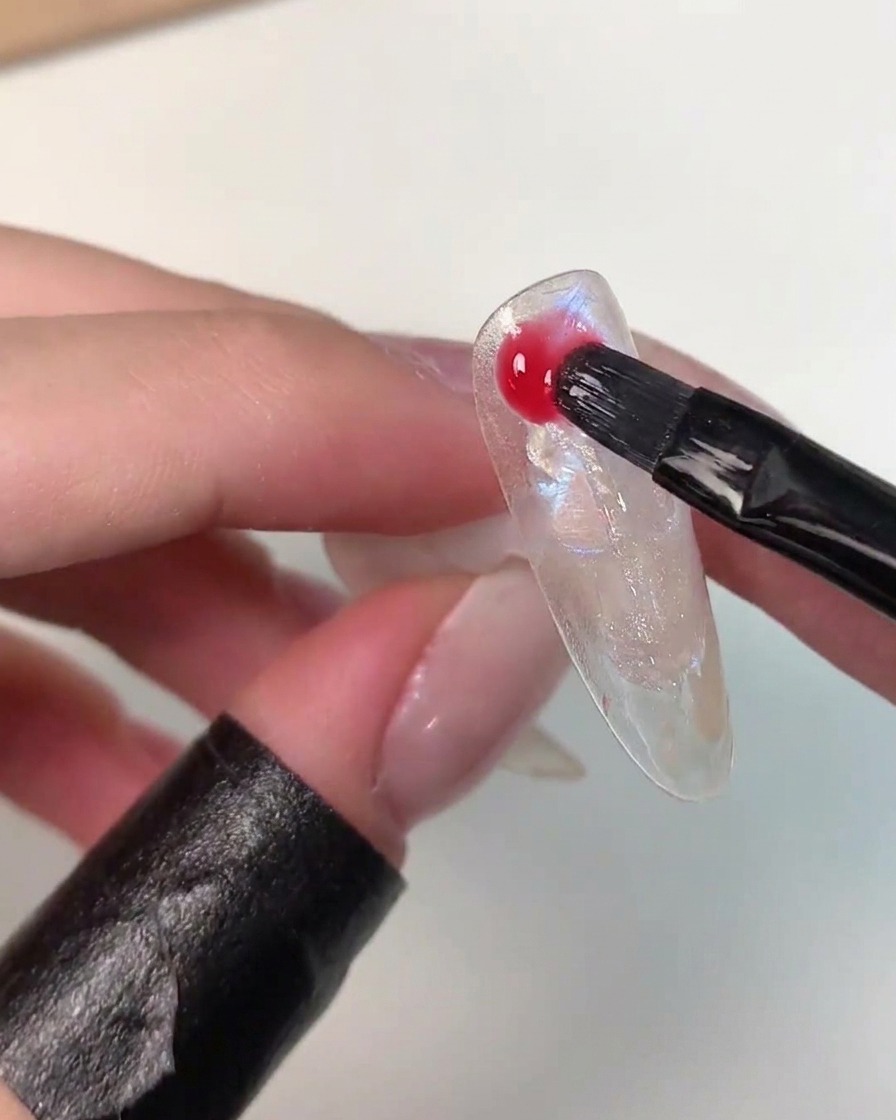 Un pincel aplicando gel de color vibrante Eiko Esaka de forma aleatoria en la superficie del arte de uñas.