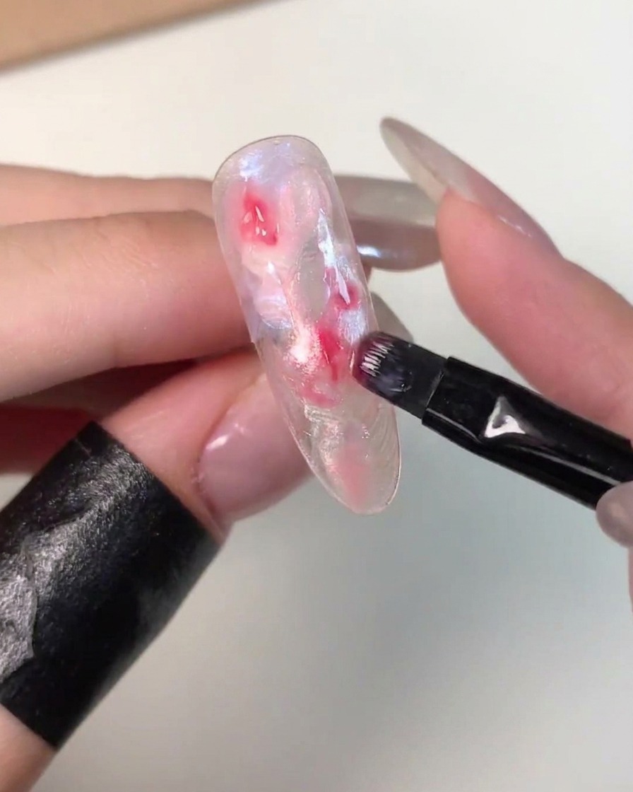 Un pincel plano pequeño aplicando gel rosa más oscuro en el centro de una punta de uña marmoleada sin curar.
