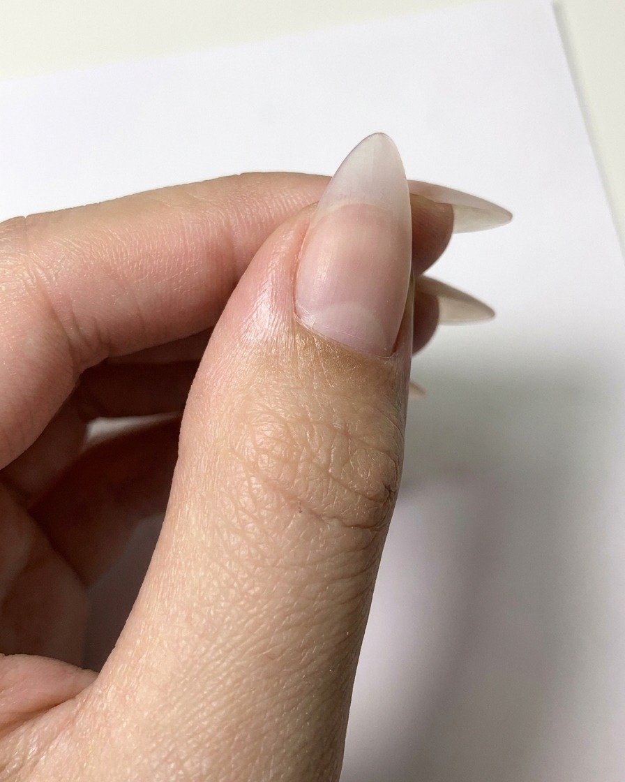 Un pincel delineador fino aplicando contornos de gel blanco sobre una superficie de uña nude mate para formar pétalos.