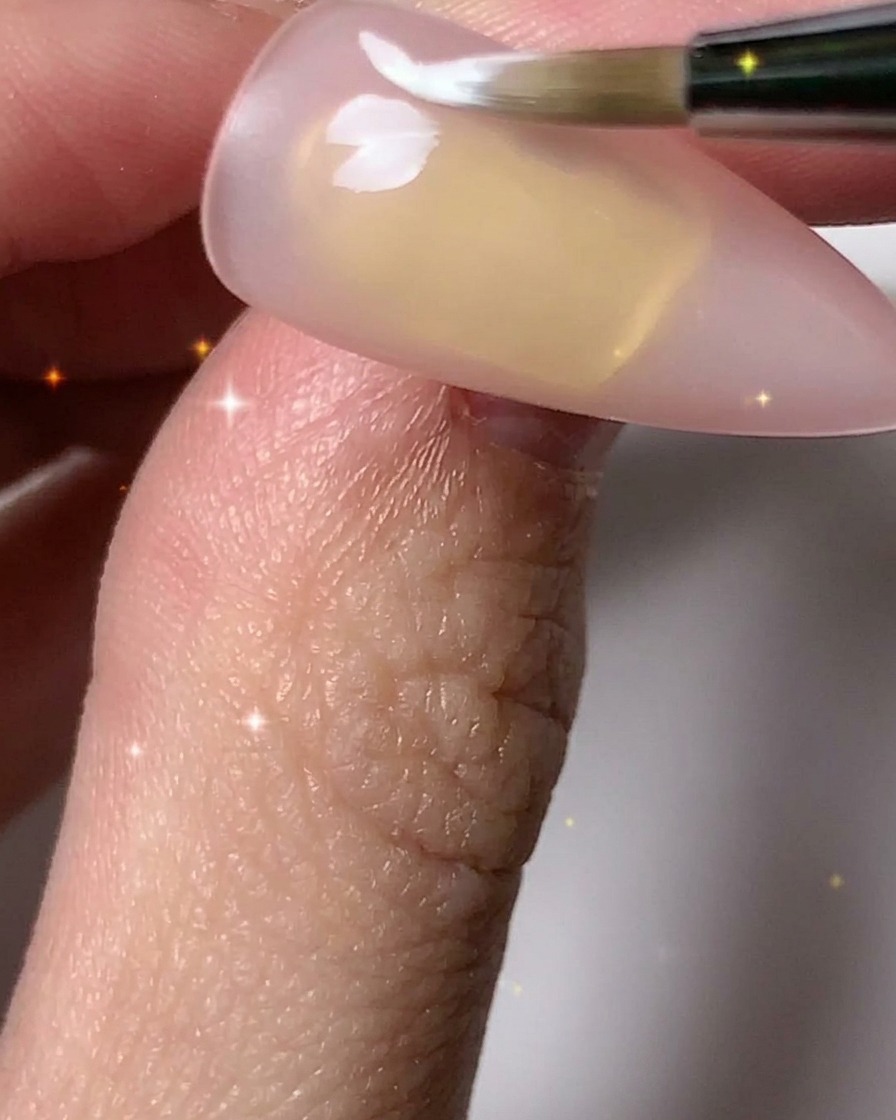 Un pincel de uñas agregando pétalos blancos para completar múltiples contornos de flores en la uña.