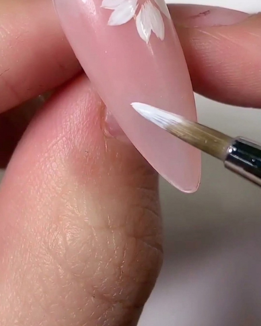 Un pincel aplicando un tinte de gel rosa claro sobre secciones de los pétalos blancos para lograr un efecto degradado.