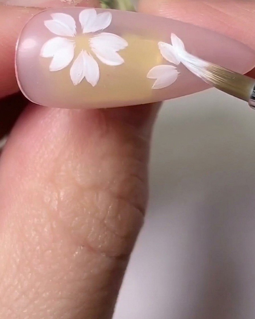 Un pincel difuminando tonos rosas y blancos en pétalos de flores de cerezo para añadir profundidad.